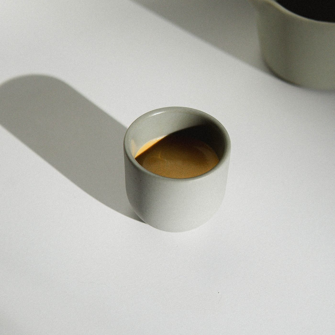 A simple coffee cup casting its shadow across a white surface in natural light.