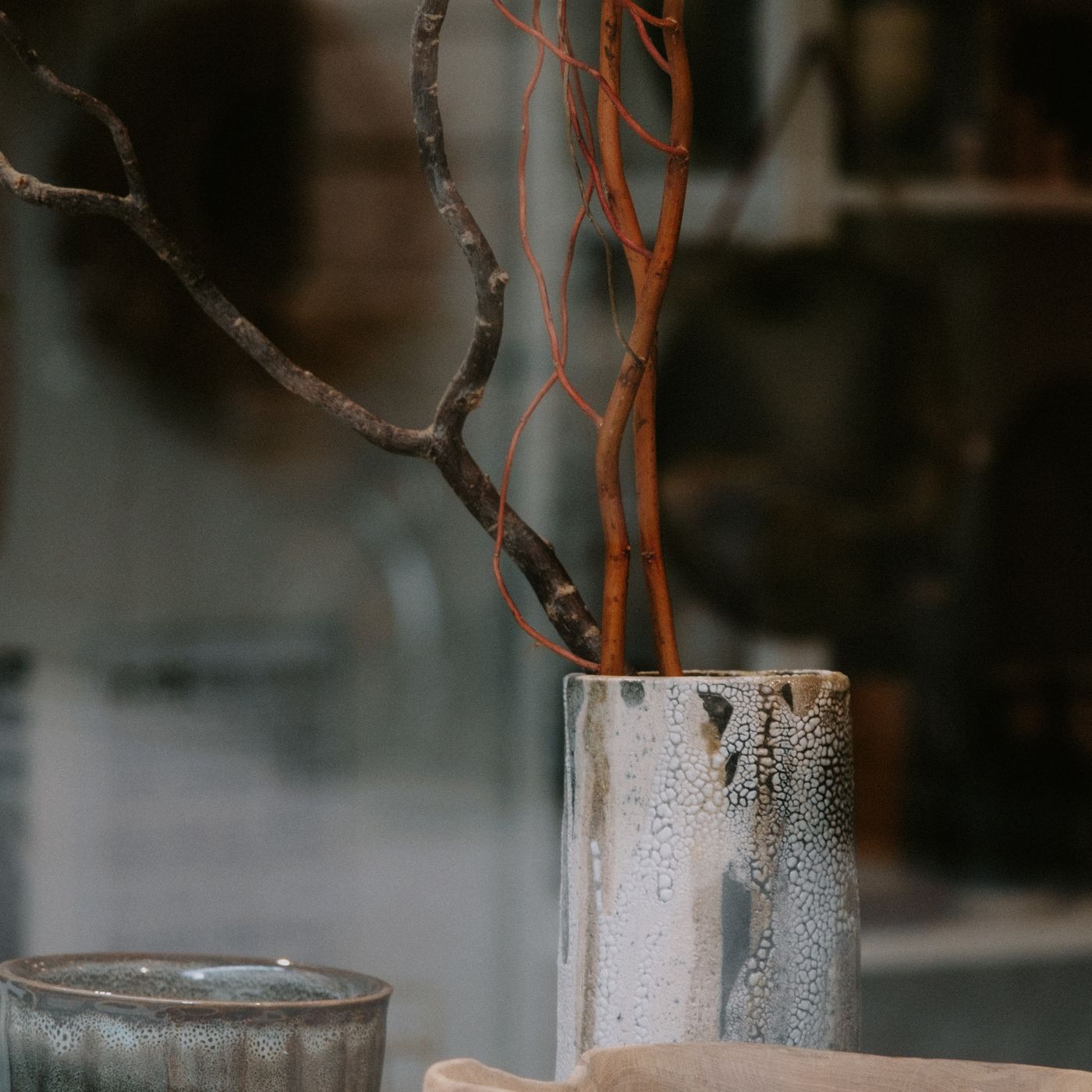 A ceramic pot holding bare branches in a plain indoor studio setting.