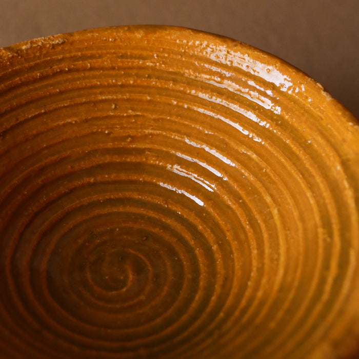 A handmade brown ceramic bowl shown close up, with a textured spiral running around the body.