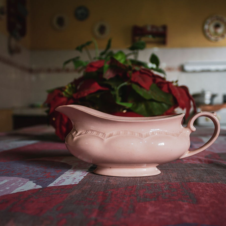 A vintage style porcelain gravy boat on a tablecloth in a kitchen.
