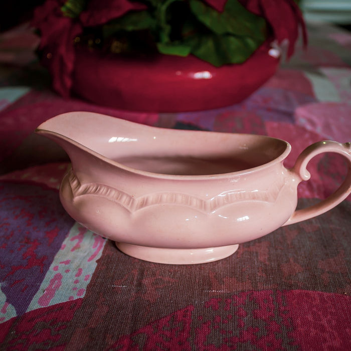 A retro pink porcelain gravy boat on a brightly coloured tablecloth indoors.