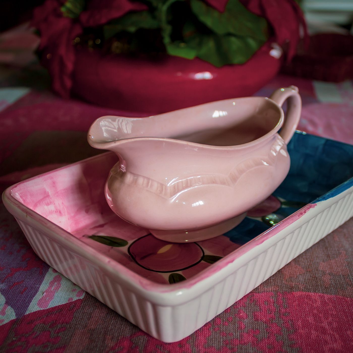 A pink porcelain saucier standing on a hand painted tray in a warm indoor setting.