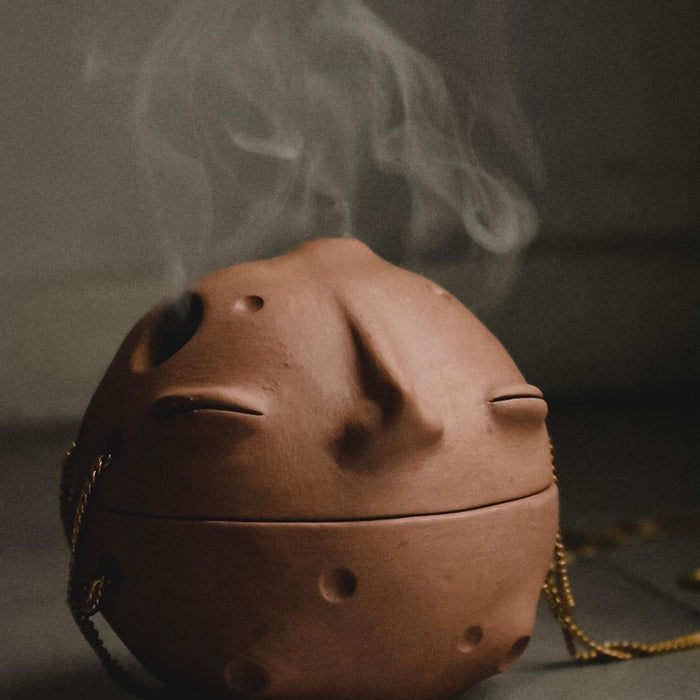A ceramic incense burner with a thin line of smoke rising from it.