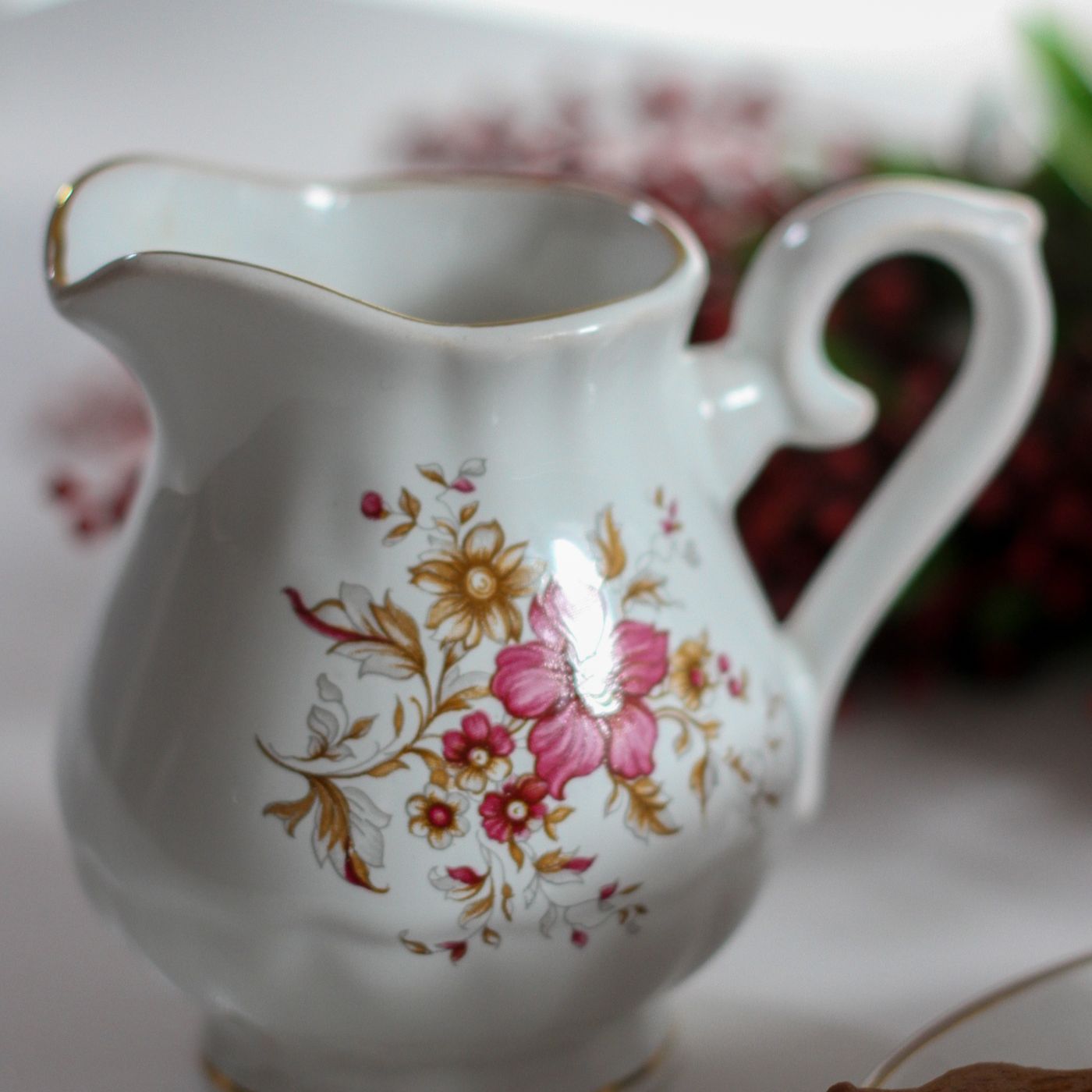 An ornate milk pot decorated with painted flowers.