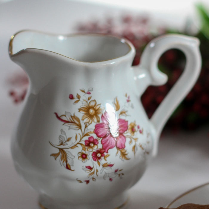An ornate milk pot decorated with painted flowers.