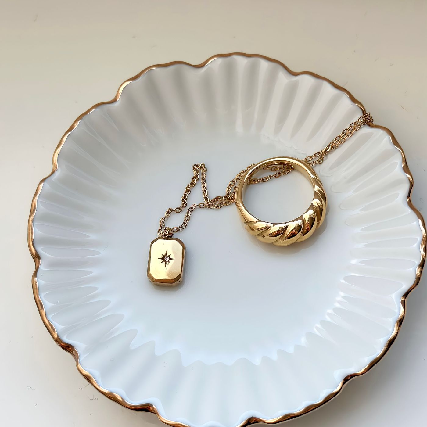 A white scalloped porcelain dish displaying a gold necklace and a ring.