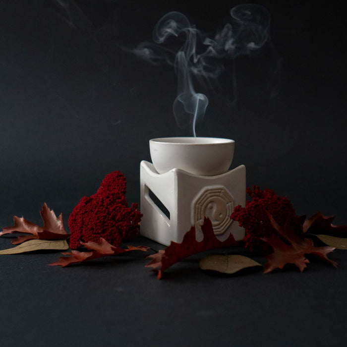 A ceramic incense burner giving off smoke, surrounded by red decorative foliage.