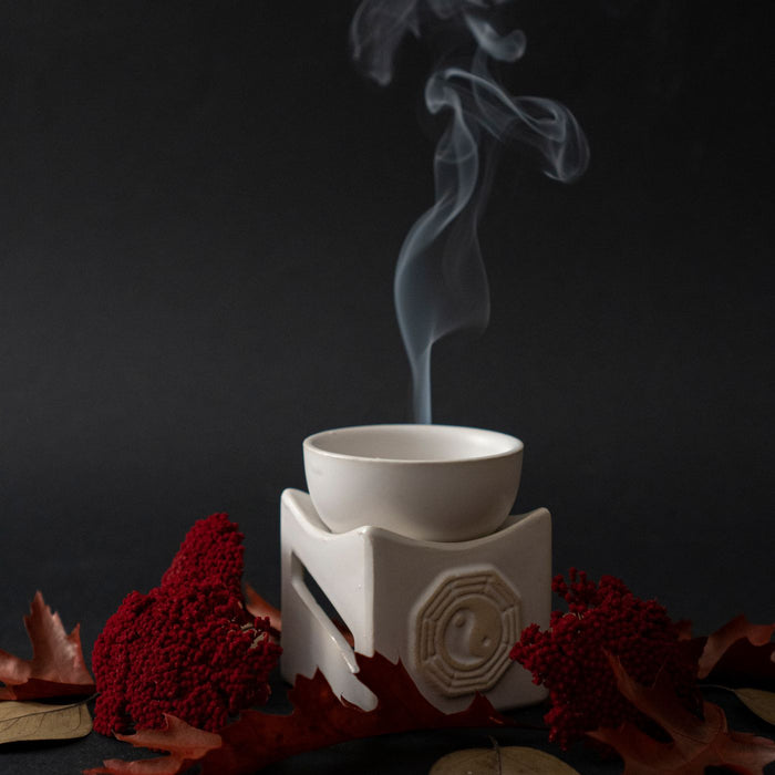 A ceramic incense burner shown with autumn leaves against a dark backdrop.