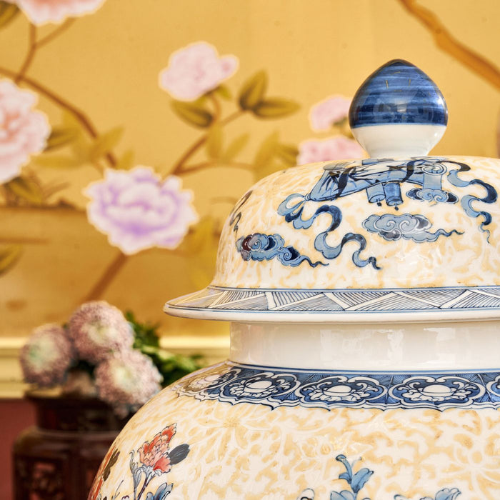 An ornate porcelain vase with classic floral designs, shown against patterned wallpaper.