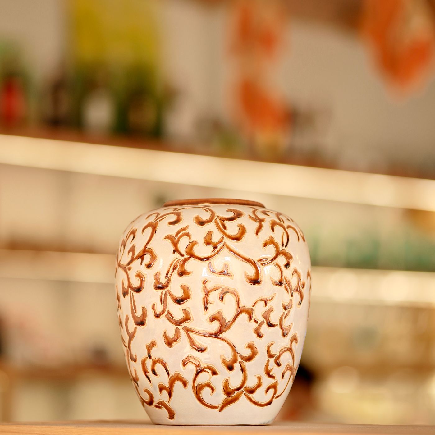 An ornate ceramic vase with a vintage style design, standing on a wooden shelf.