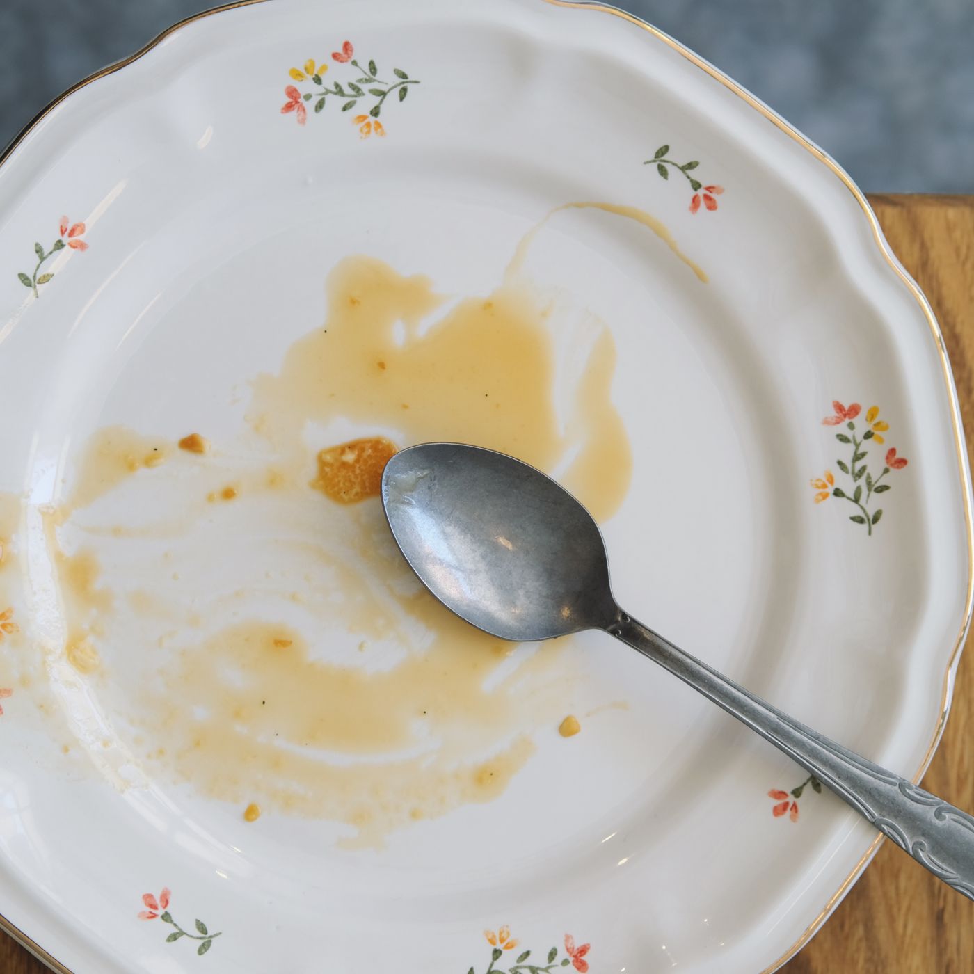 An empty decorative plate on a wooden table with a spoon resting next to it.