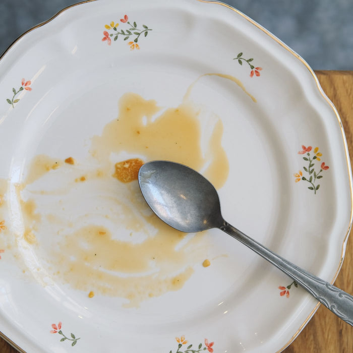 An empty decorative plate on a wooden table with a spoon resting next to it.