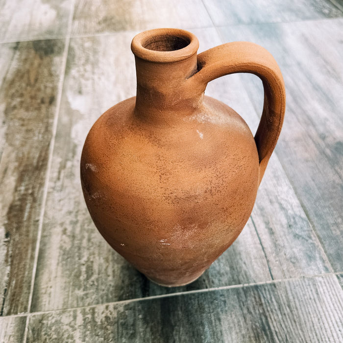 A rustic terracotta jug photographed close up on a textured floor.