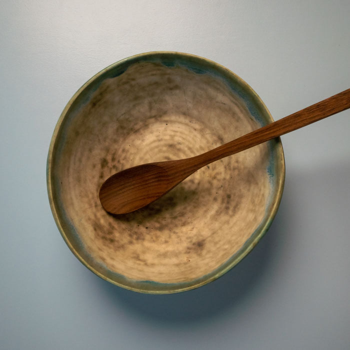 A beige bowl seen from above on a white table with a wooden spoon laid beside it.