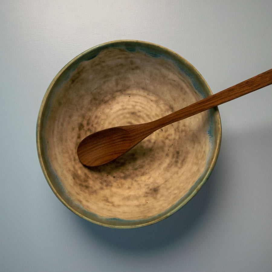 A beige bowl seen from above on a white table with a wooden spoon laid beside it.