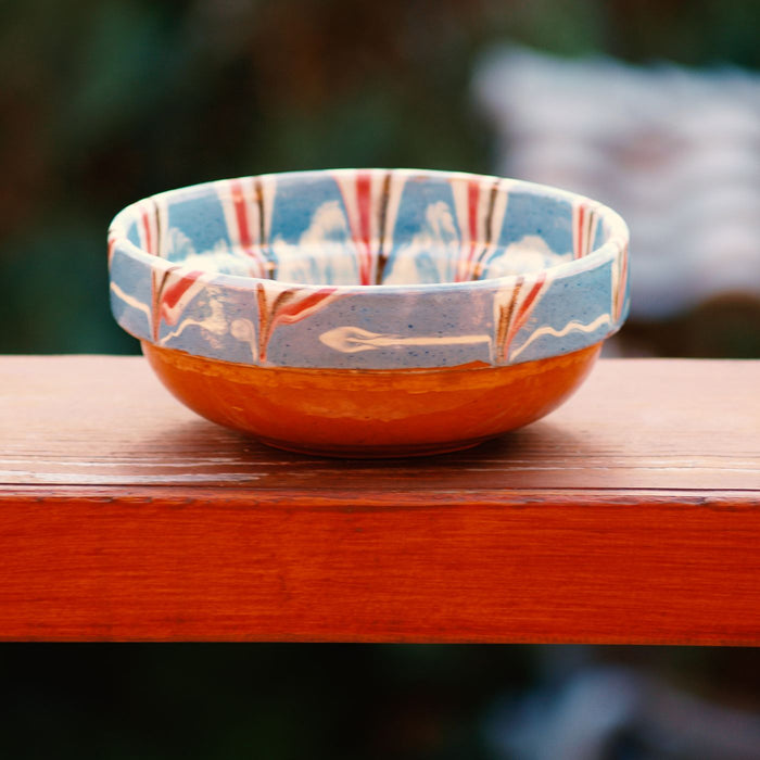 A brightly patterned ceramic bowl photographed outdoors on a wooden table.