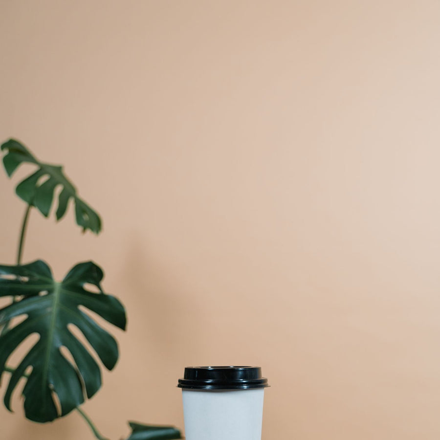 A white cup fitted with a black lid, standing on a wooden table against a beige background.