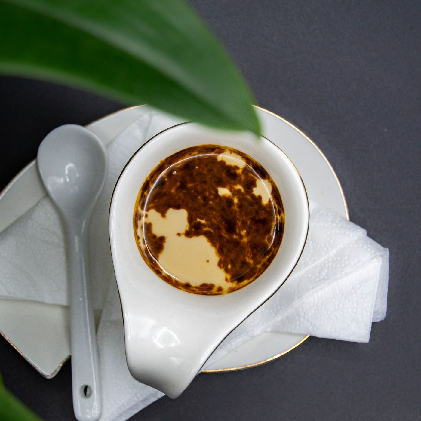 A ceramic gravy boat holding oil, standing beside a ceramic saucer with a spoon on it.