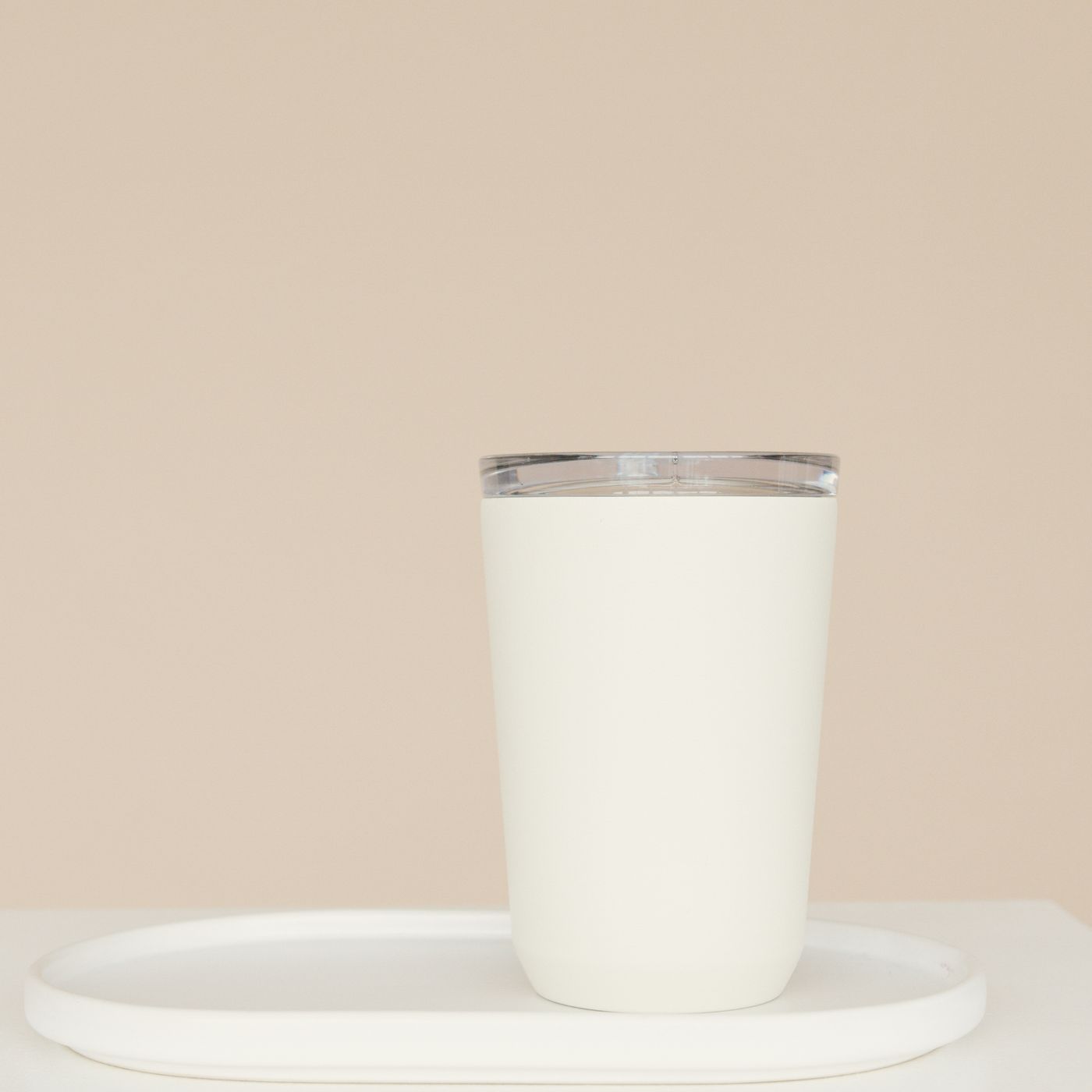 A white cup resting on a plain tray against a neutral beige backdrop.