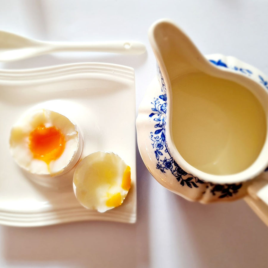 A ceramic gravy boat photographed close up beside an egg.