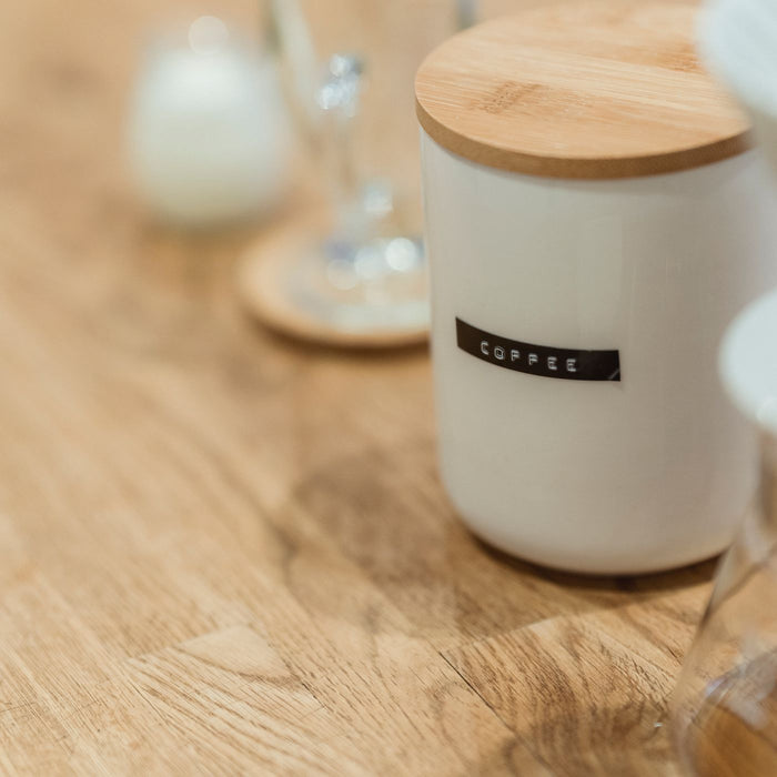 A ceramic coffee jar with a wooden lid, photographed close up on a table.