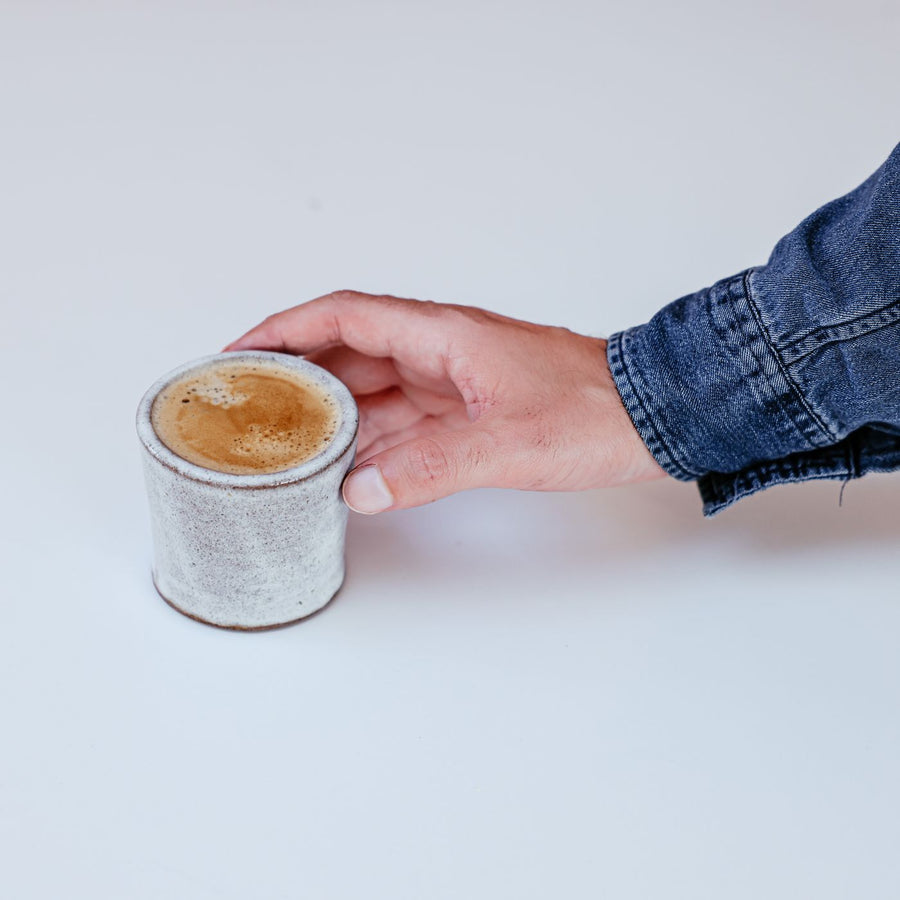 A ceramic cappuccino cup being lifted by hand against a white background.