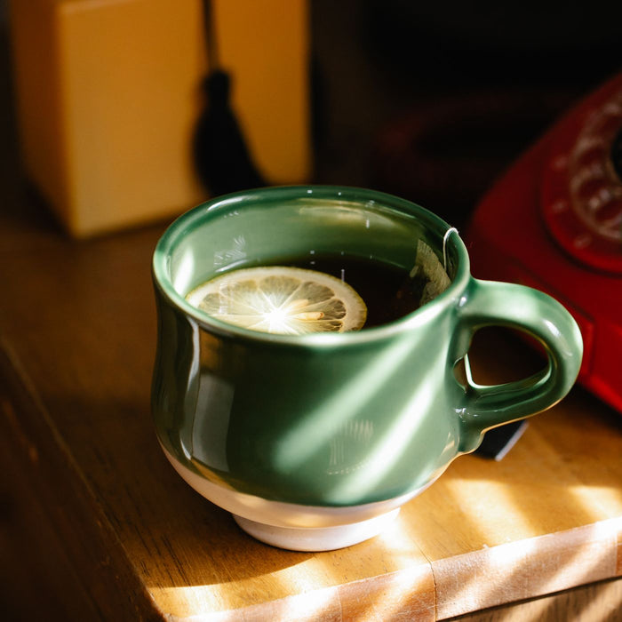 A green mug in warm natural light with lemon tea sitting in it.