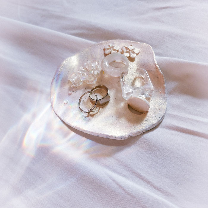A ceramic dish photographed from above with jewellery and crystals arranged across it.