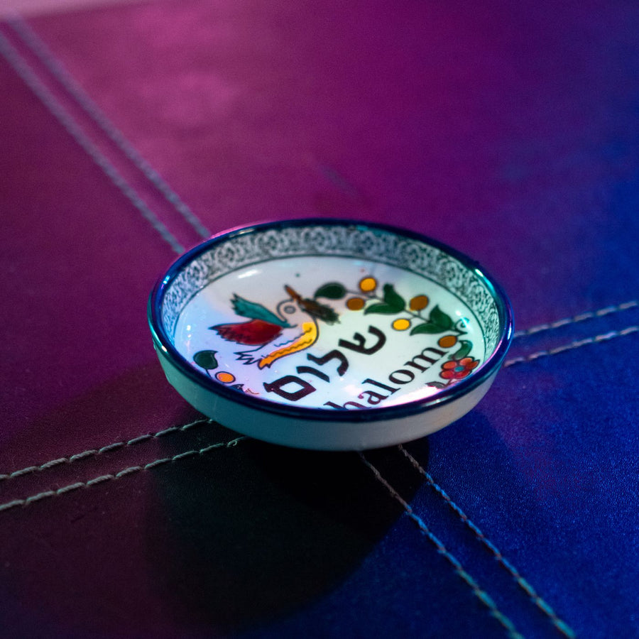 A colourful ceramic saucer lettered Shalom, photographed close up under night lights.